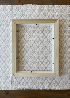 an empty wooden frame sitting on top of a table next to a wallpapered wall