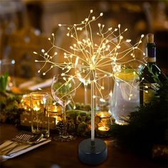 a table topped with wine glasses and a light up tree centerpiece on top of a wooden table