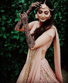 a woman in a pink lehenga holding her hands up to her face and looking at the camera