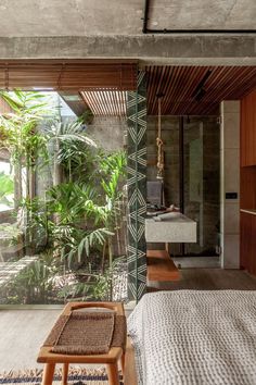 a bedroom with a bed, table and plants in the room next to it's glass walls