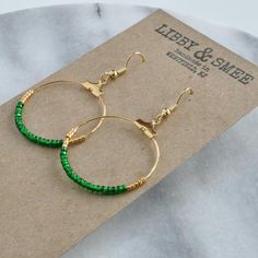 Your soon-to-be favorites, these small gold beaded hoops (available in 16 exclusive patterns) are perfect for day, night and well, everything in between. + beaded hoops with tiny glass emerald green beads and gold glass Delica beads+ gold-plated hoop and hooks (lead-free and nickel-free)+ comes with plastic earring back for security+ circle is approximately 1.25" in diameter and overall length is about 2" from top of hook+ packaged on a hand-stamped kraft earring card in a clear resealing bag ma Adjustable Hoop Earrings With Gold Beads As Gift, Adjustable Gold Beads Hoop Earrings As Gift, Adjustable Gold Beaded Hoop Earrings As Gift, Small Hoop Gold Beaded Earrings For Gifts, Green Beaded Earrings, Green Statement Earrings, Irish Earrings, Green Earring, Geode Jewelry