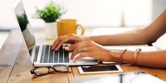 a woman is typing on her laptop while sitting at a table with coffee and other items