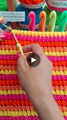 someone is crocheting with yarn and knitting needles in front of some colorful items