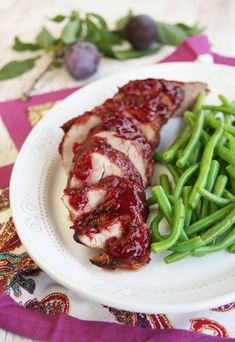 a white plate topped with meat and green beans on top of a purple table cloth