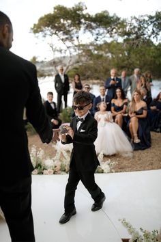 a little boy in a tuxedo walking down the aisle