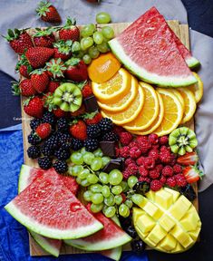 a wooden cutting board topped with watermelon, oranges, and other fruits