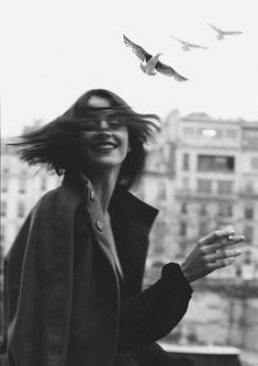 a woman standing on top of a roof with birds flying above her and buildings in the background