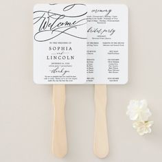 two fan shaped wedding programs on top of each other next to a small white flower