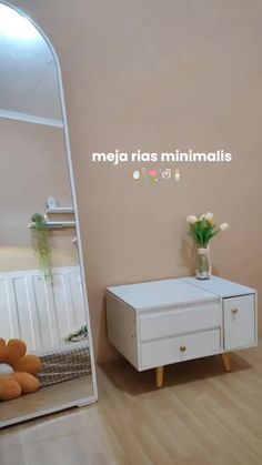 a white dresser sitting next to a mirror on top of a wooden floor