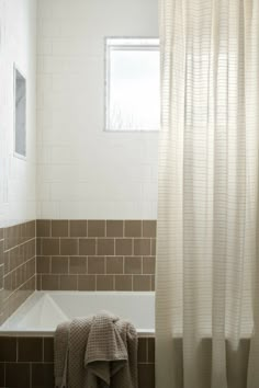 a bath tub sitting under a window next to a white shower curtain and tiled floor