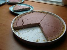 there is a chocolate pie on the table next to two plates with slices cut out