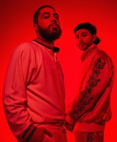 two men standing next to each other in front of a red background with the same color