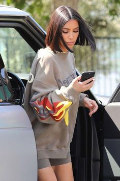 a woman in grey sweatshirt and shorts looking at her cell phone while stepping out of a car