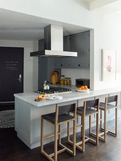 a kitchen with white counter tops and wooden stools in front of an island topped with fruit