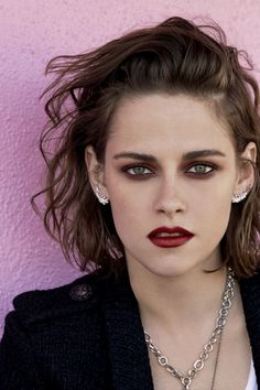 a woman with red lipstick and piercings posing for a photo in front of a pink wall