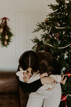 a woman is hugging her child in front of a christmas tree with presents on it