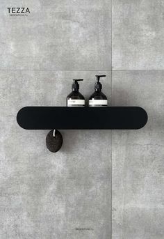 two soap dispensers sitting on top of a black shelf next to a gray wall