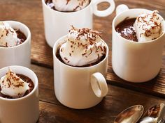 four white mugs filled with hot chocolate and marshmallows on top of a wooden table