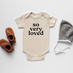 a baby bodysuit with the words first edition and two pairs of shoes next to it