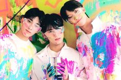 three young men standing next to each other in front of a wall with colorful paint on it