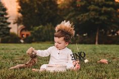 a baby sitting in the grass wearing a mohawk