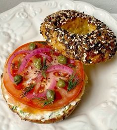 a bagel sandwich with tomatoes, onions and sprouts on it sitting on a white plate