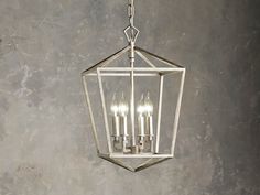 three lit candles are hanging from a metal caged light fixture on a concrete wall