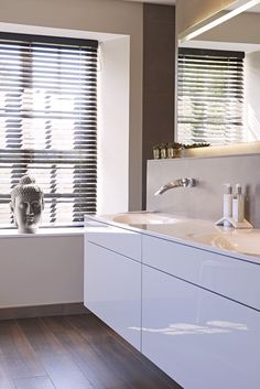 a white bathroom with two sinks and a large window that has blinds on it's side