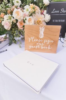 a wooden sign sitting on top of a white table next to flowers and other items