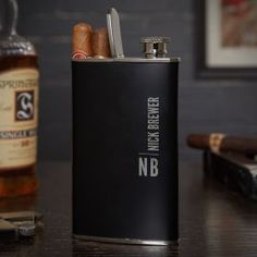 a black flask with two cigars in it next to a bottle of whiskey