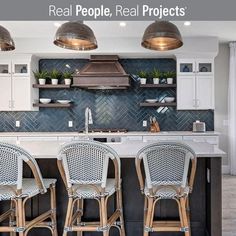 three chairs are sitting at the center of this kitchen island with marble countertops and stainless steel pendant lights