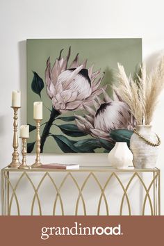 a painting on the wall above a console table with candles and flowers in vases