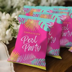 three pink and blue party bags sitting on top of a table next to white flowers