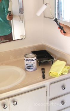 a person using a brush to paint a bathroom vanity with white cabinets and countertop