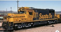 a yellow and black train engine sitting on the tracks next to some power lines with mountains in the background