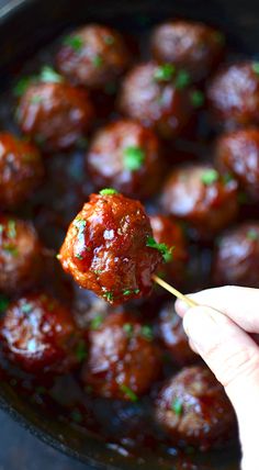 a hand holding a piece of meatball on a toothpick in a skillet