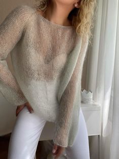 a woman in white pants and a sweater posing for the camera with her hands on her hips