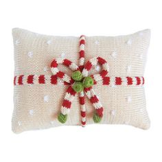 a knitted christmas pillow with candy canes and holly on the front, sitting on a white surface