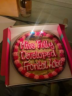 a birthday cake with pink frosting in a box on a table next to a wine bottle