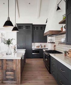 a large kitchen with black cabinets and white counter tops, wooden flooring and hanging lights