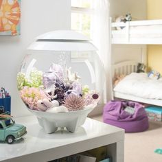 there is a fish bowl with flowers in it on top of a white table next to a bunk bed