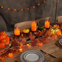 a wooden table topped with plates covered in pumpkins next to candles and fall leaves