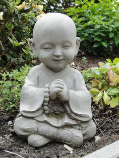 a small buddha statue sitting on top of a dirt ground in front of some bushes