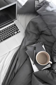 a laptop computer sitting on top of a bed next to a cup of coffee and notebook