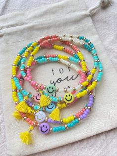 three bracelets with smiley faces and tassels on them, one is for you