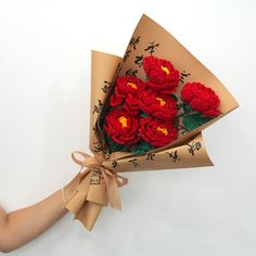 a bouquet of red flowers wrapped in brown paper with writing on the side and ribbon