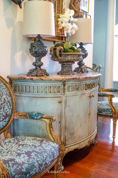 an antique dresser with two lamps on top and a blue chair in the foreground