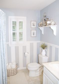 a white toilet sitting in a bathroom next to a sink and shower curtain with shutters on the window