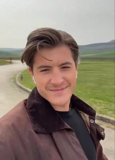 a young man smiling at the camera in front of an empty road and grassy field