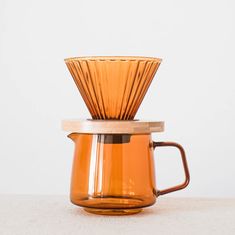 an orange coffee pot sitting on top of a table next to a wooden strainer